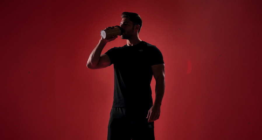 foto de um homem em uma sala com o fundo vermelho tomando beef protein sabor cacau com 24g de proteína