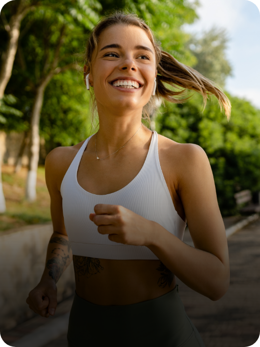 Uma mulher com roupa esportiva segurando potes de creatina em goma com os sabores jabuticaba, laranja e maçã verde, da essential nutrition.