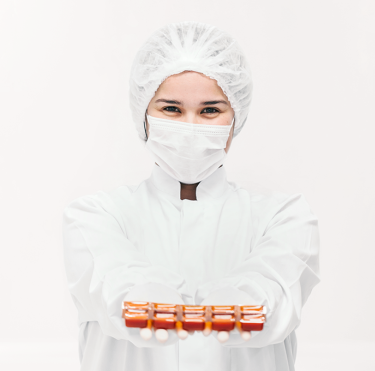 Mulher com roupa completa de laboratório de manipulação de medicamentos, segurando nas mãos gomas de colágeno à base de gelatina manipuladas pela Essentia Pharma